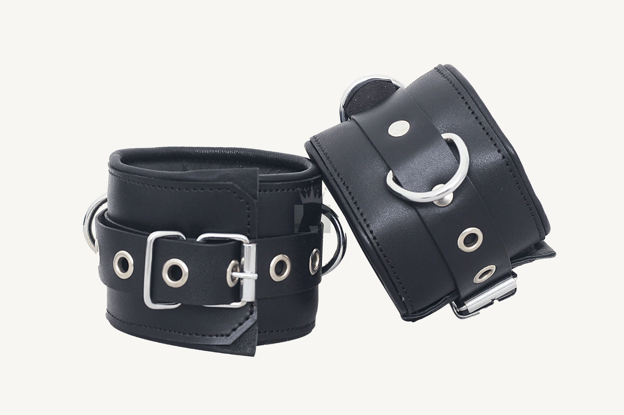 A set of black leather bondage handcuffs with metal buckles and eyelets, arranged on a white surface.