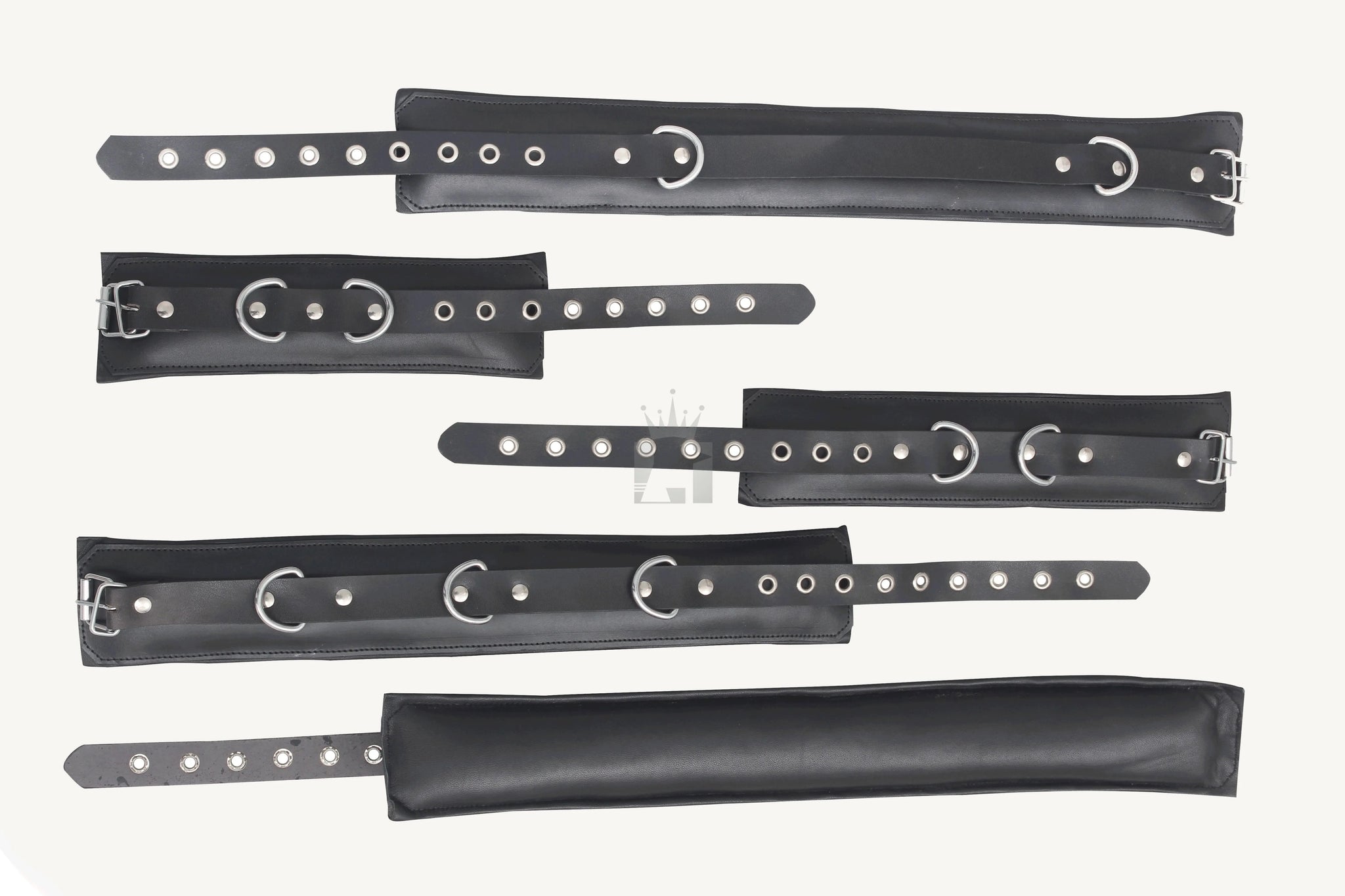 A set of black leather bondage handcuffs with metal buckles and eyelets, arranged on a white surface.