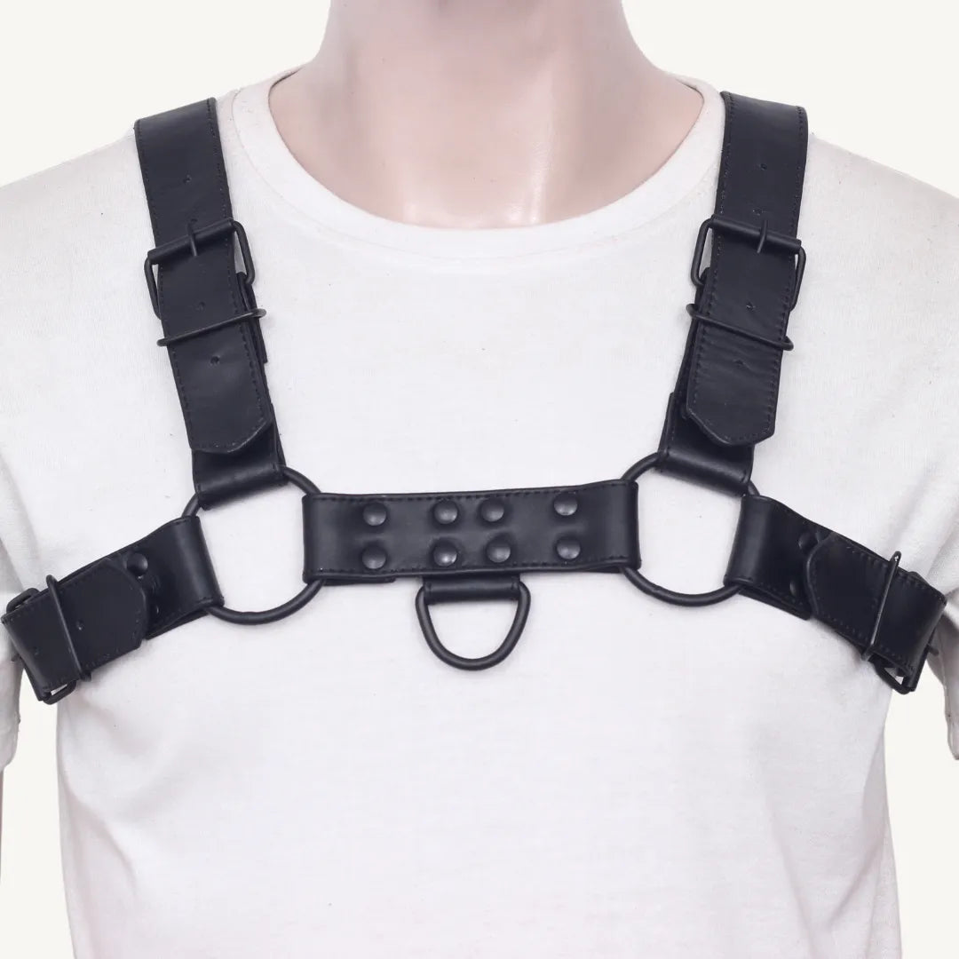 Straight front view of black leather chest harness with riveted design and metal rings on straps.