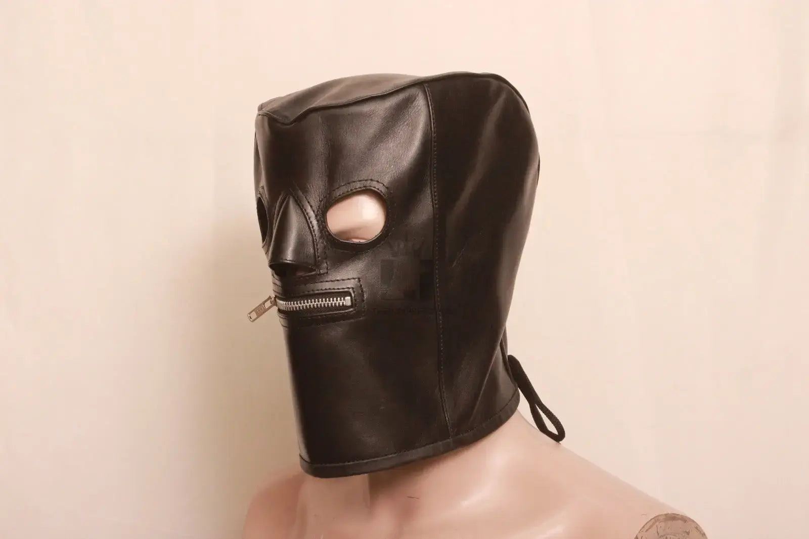  Side angle view of a dummy wearing a black leather bondage hood with a mouth zipper and laces on a white background.