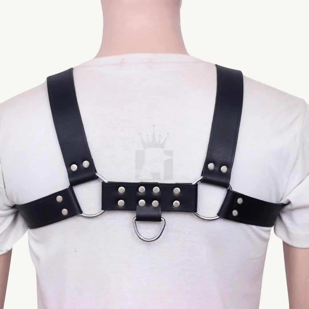 Rear view of black leather chest harness with riveted back strap and dual O-rings on white shirt.