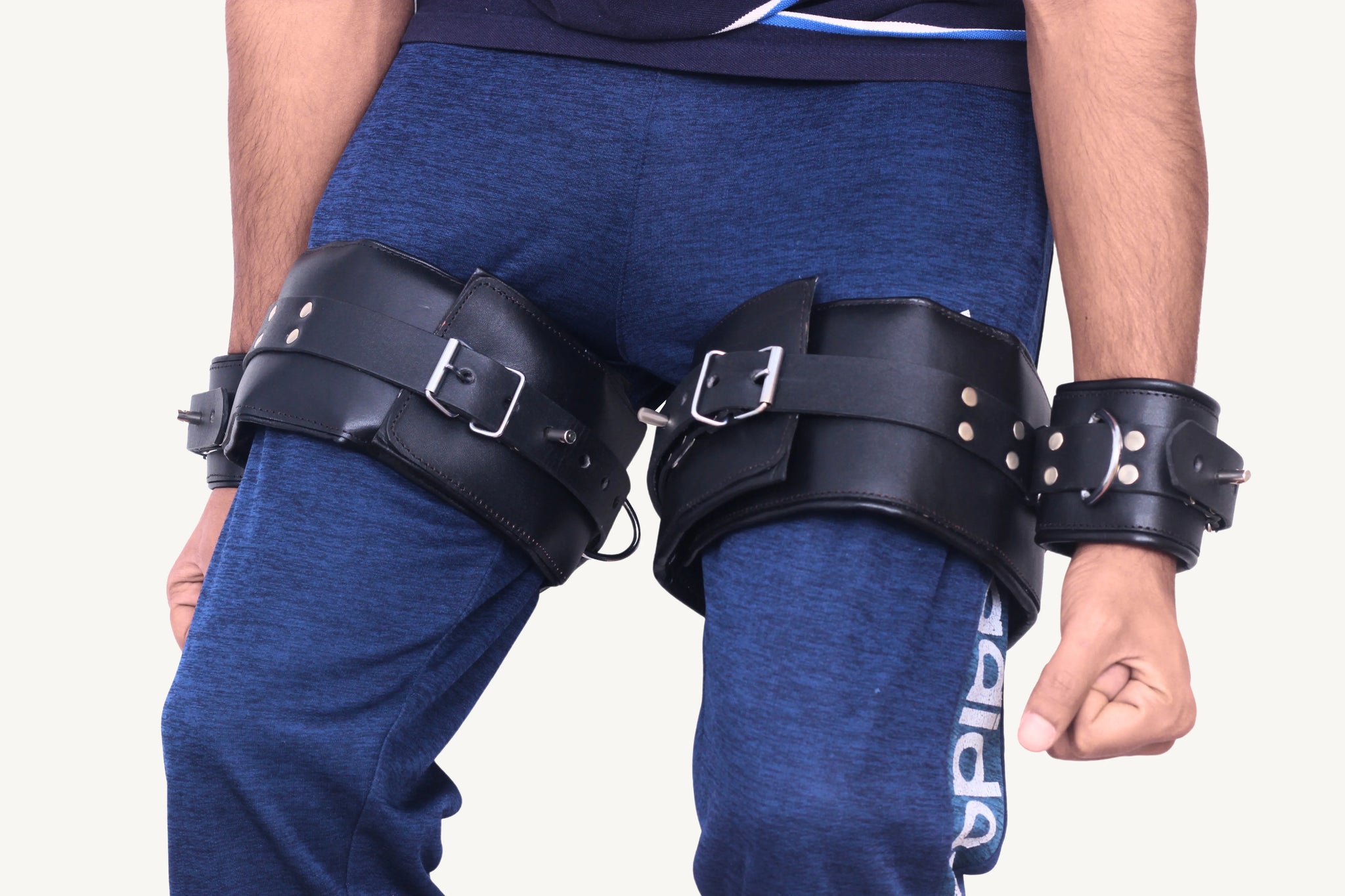 Front-facing view of a person wearing black leather thigh-to-wrist bondage cuffs with adjustable buckles