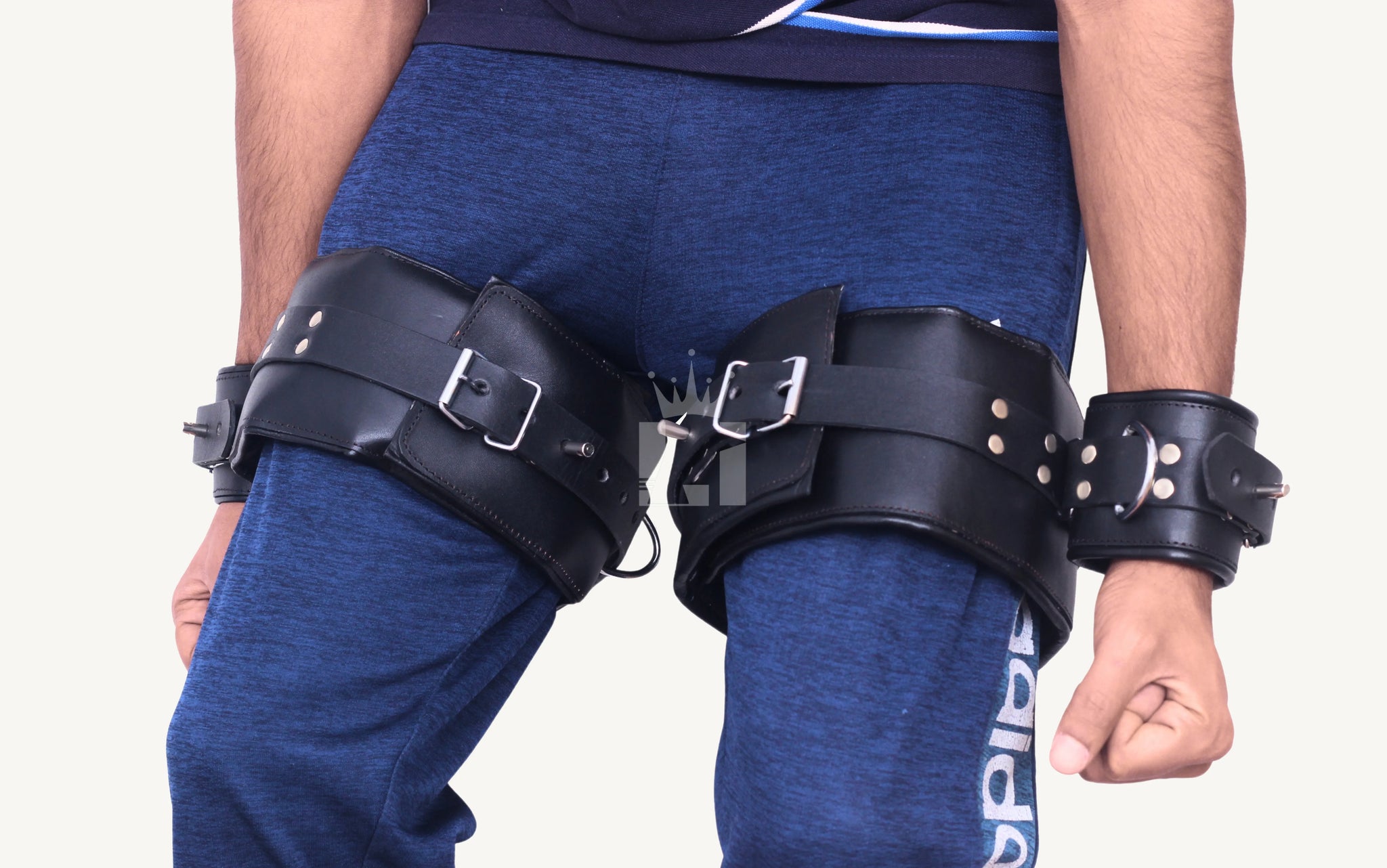 Front-facing view of a person wearing black leather thigh-to-wrist bondage cuffs with adjustable buckles