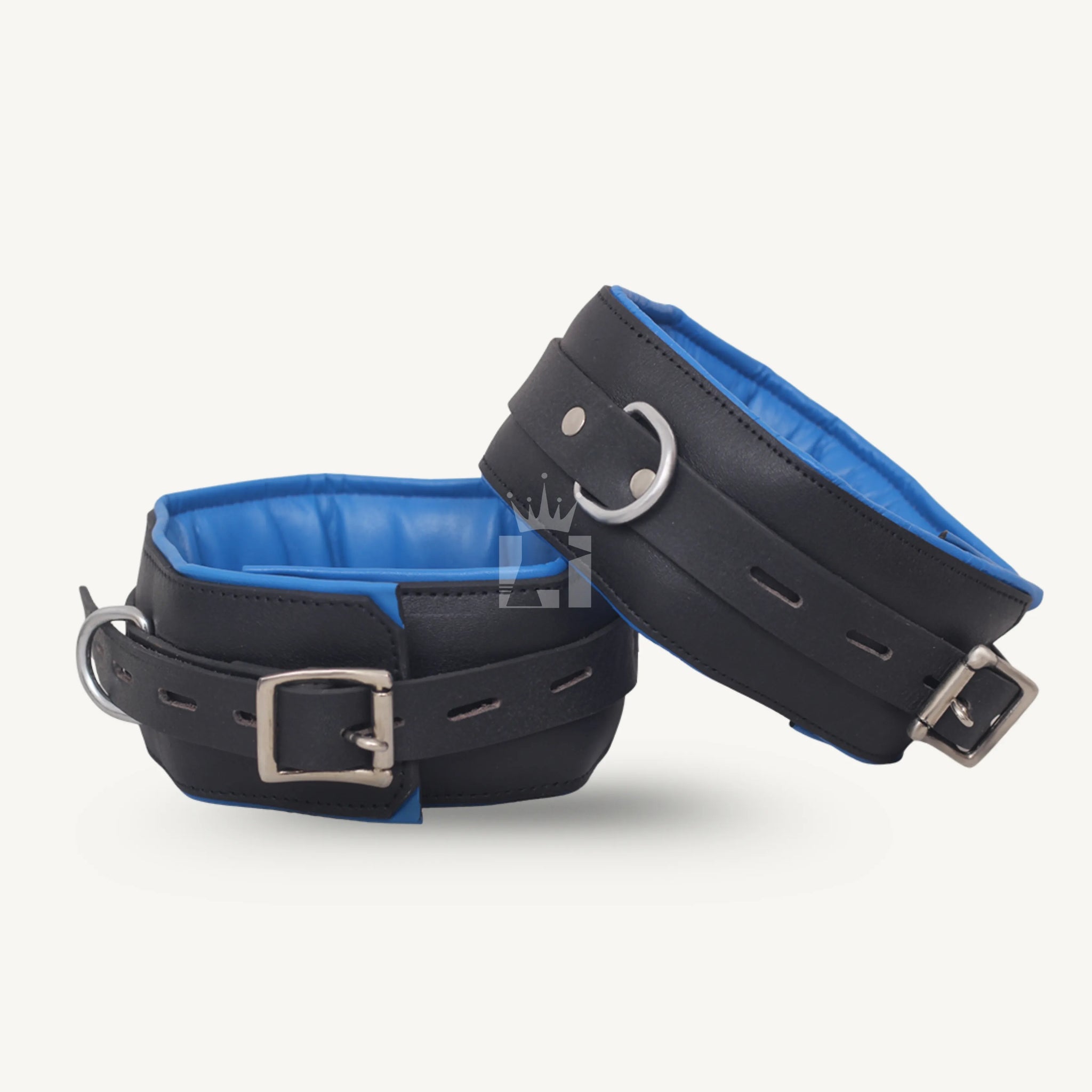 Pair of thigh cuffs in black leather with blue padding, adjustable buckles, and steel D-rings for secure bondage use.