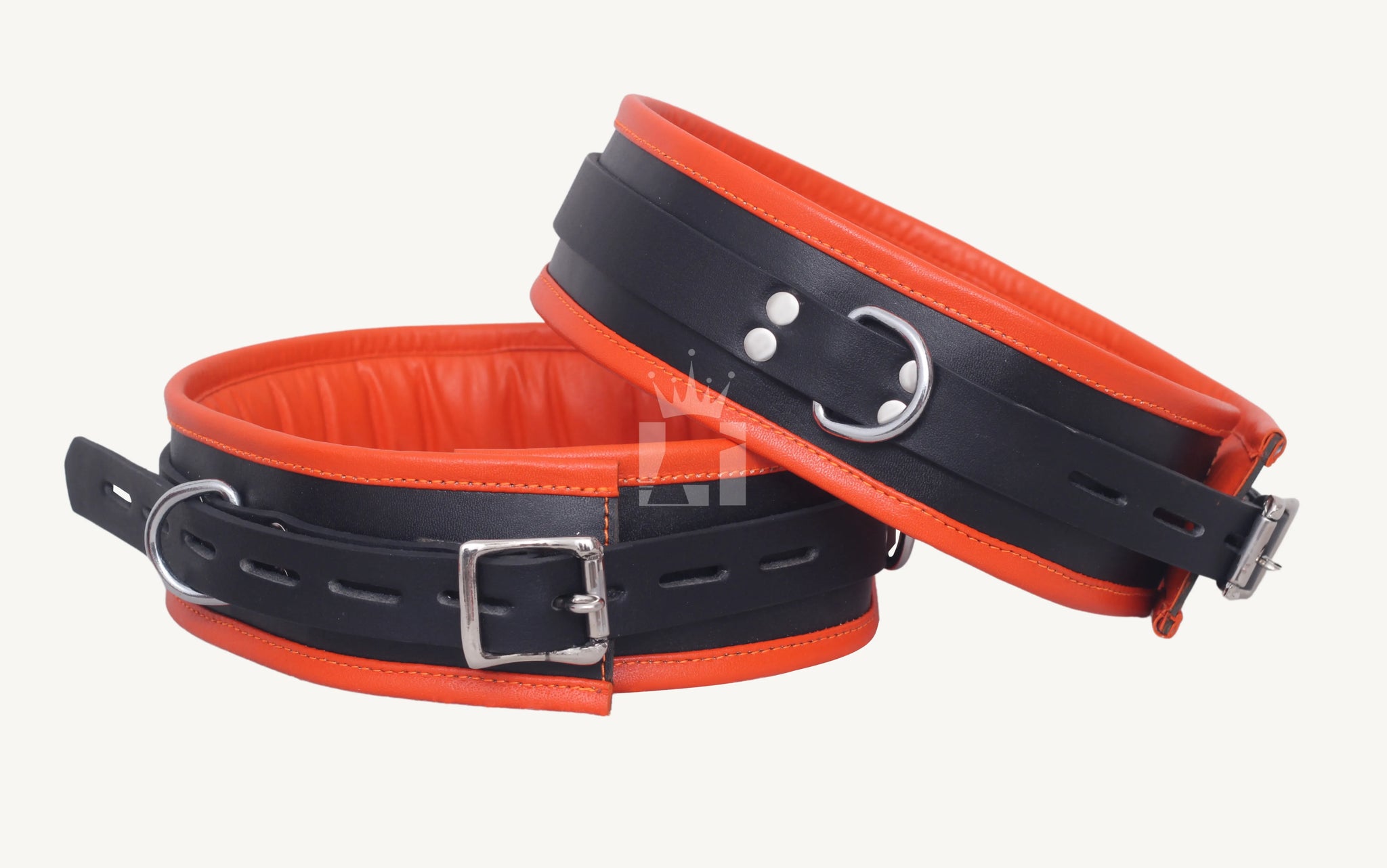 Close-up angled view of two black and orange leather thigh cuffs, one front-facing with buckle, the other tilted showing D-ring