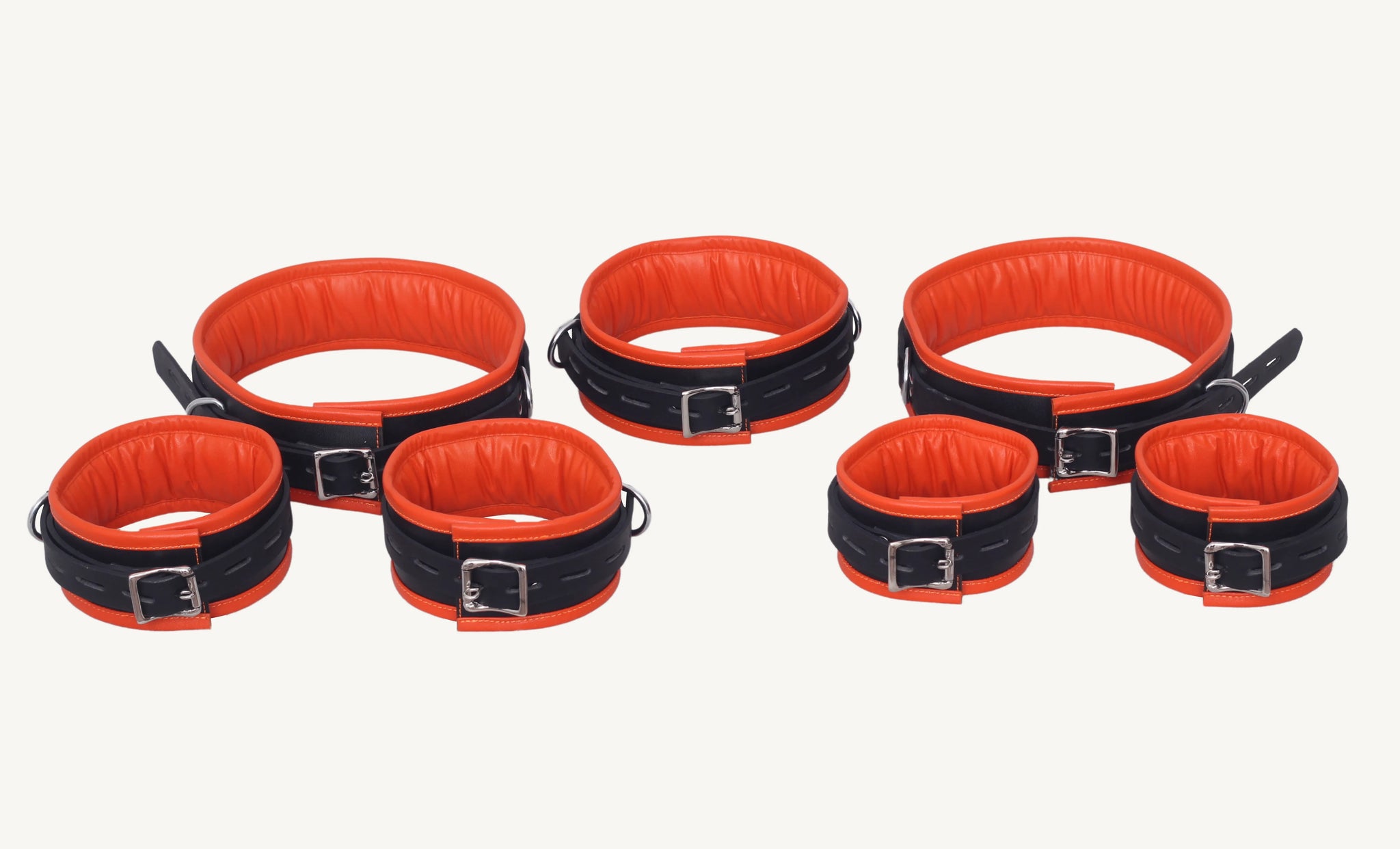 Angled top view of complete black and orange leather bondage cuffs set arranged with all cuffs and collar