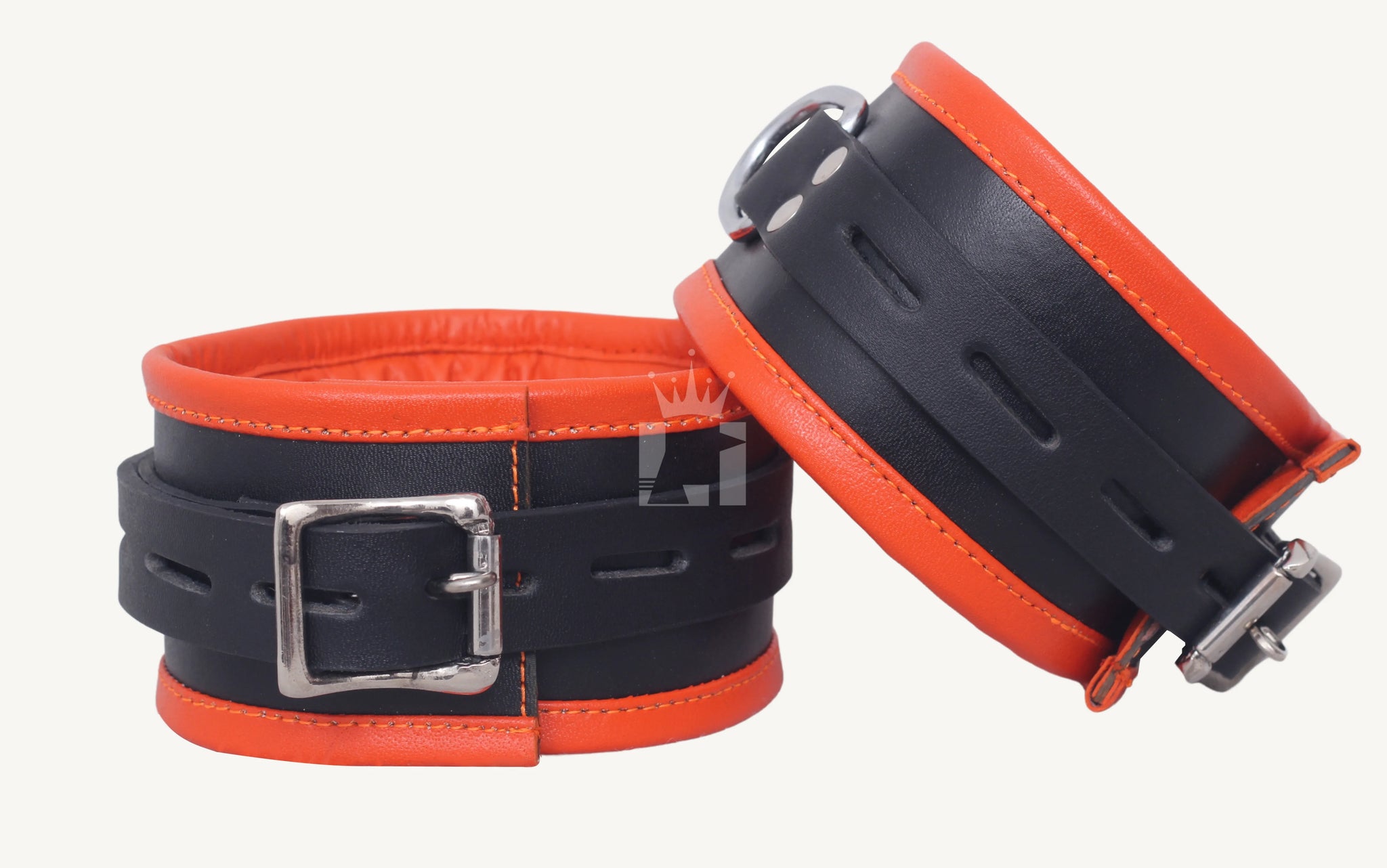 Front-facing view of two black and orange leather handcuffs, one upright showing the buckle, the other angled to display the side profile.