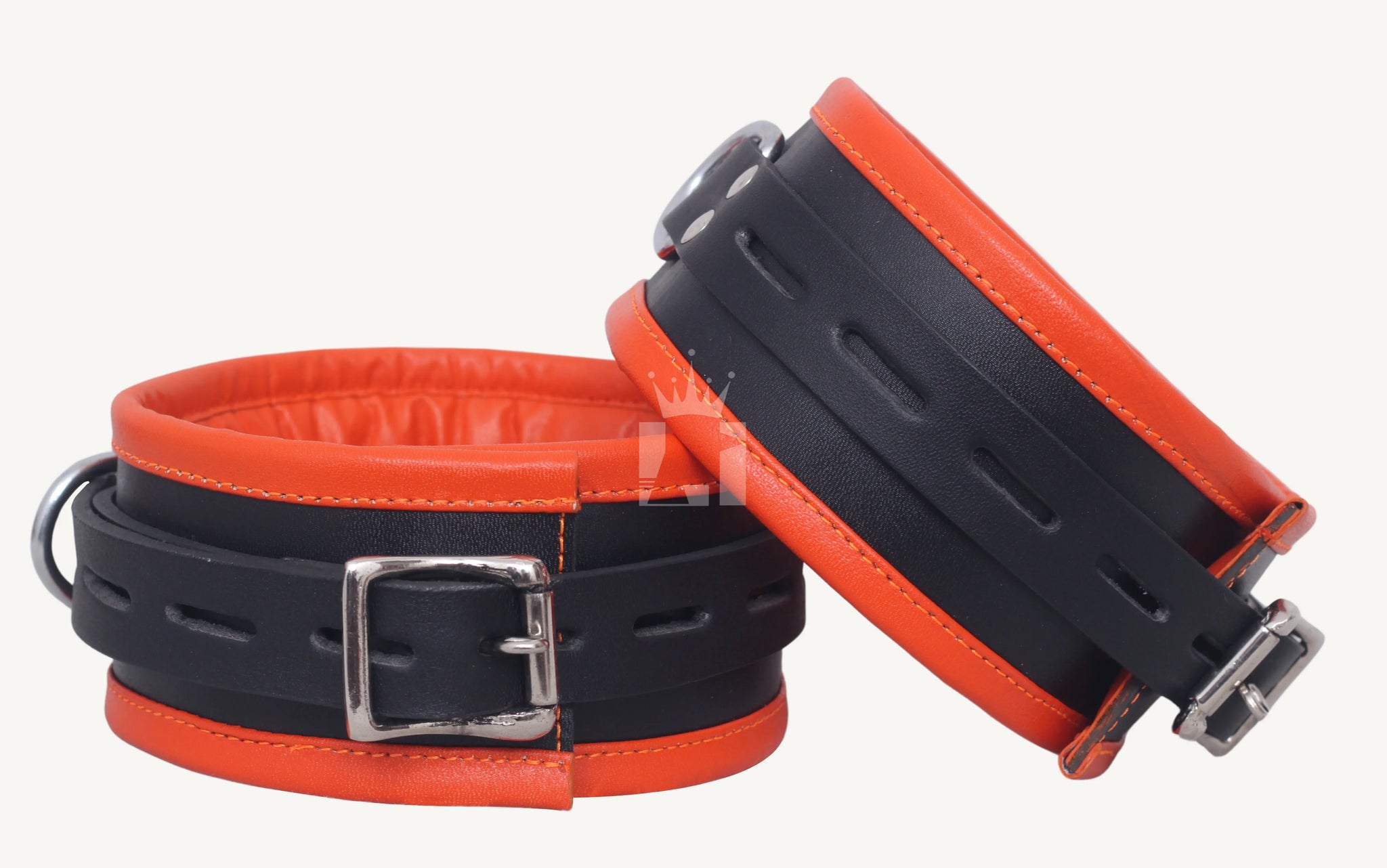 Close-up front view of two black and orange leather thigh cuffs, one upright showing the buckle, the other angled to highlight strap holes and closure.