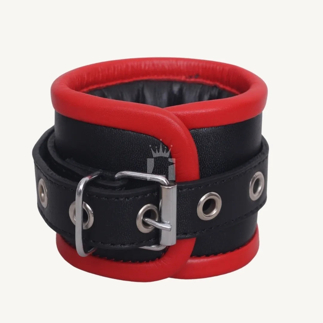 Close-up angled front view of a black and red leather handcuff with padded edges, buckle, and reinforced eyelets