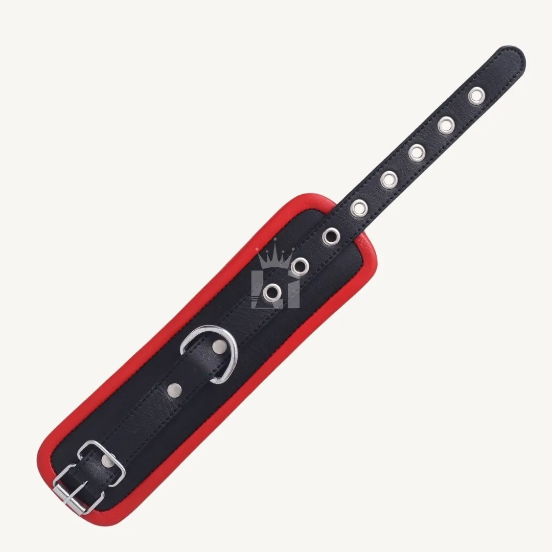 Top-down flat lay view of a black and red leather handcuff with metal buckle, eyelets, and D-ring