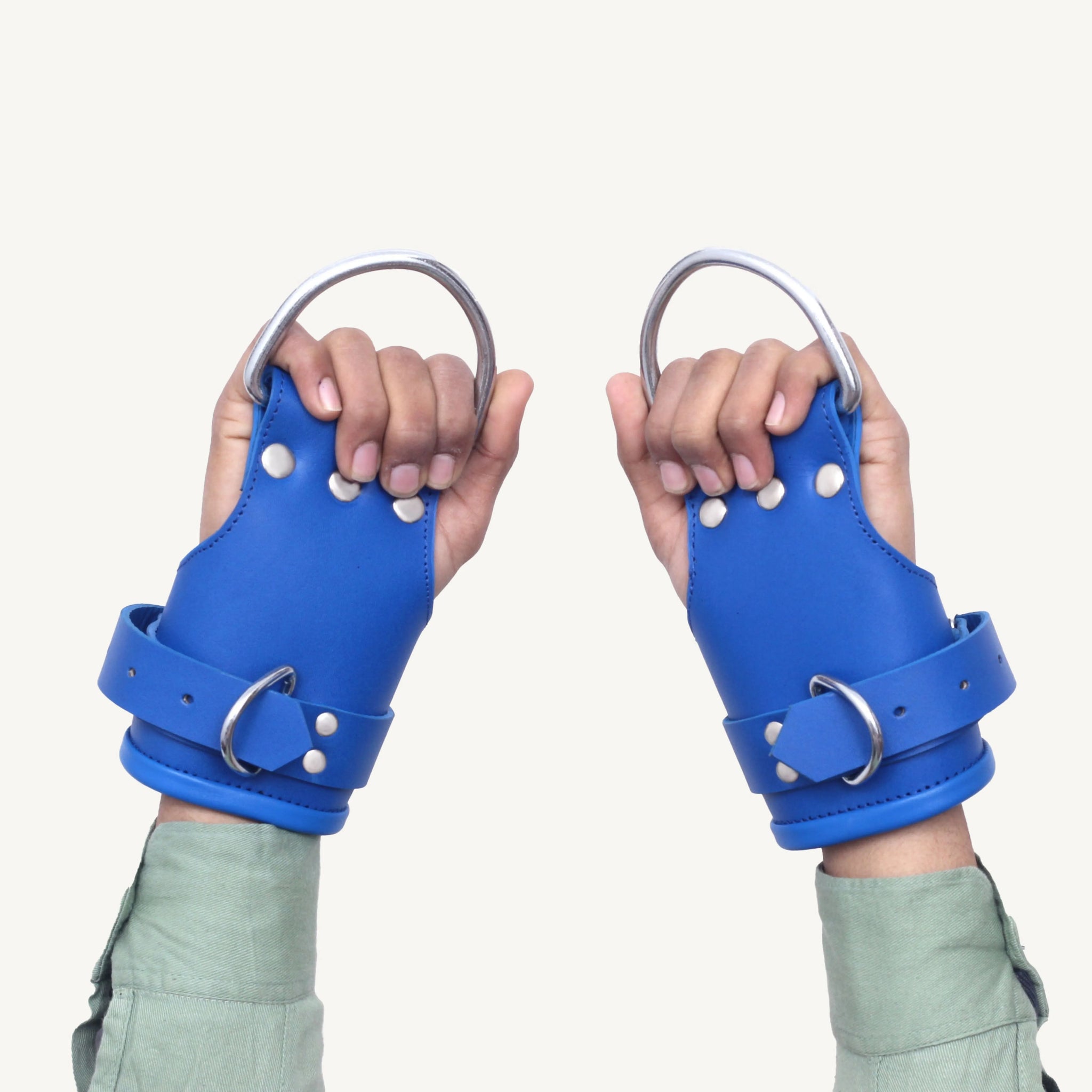 Pair of blue leather wrist suspension cuffs with metal D-rings, worn on hands for secure restraint.