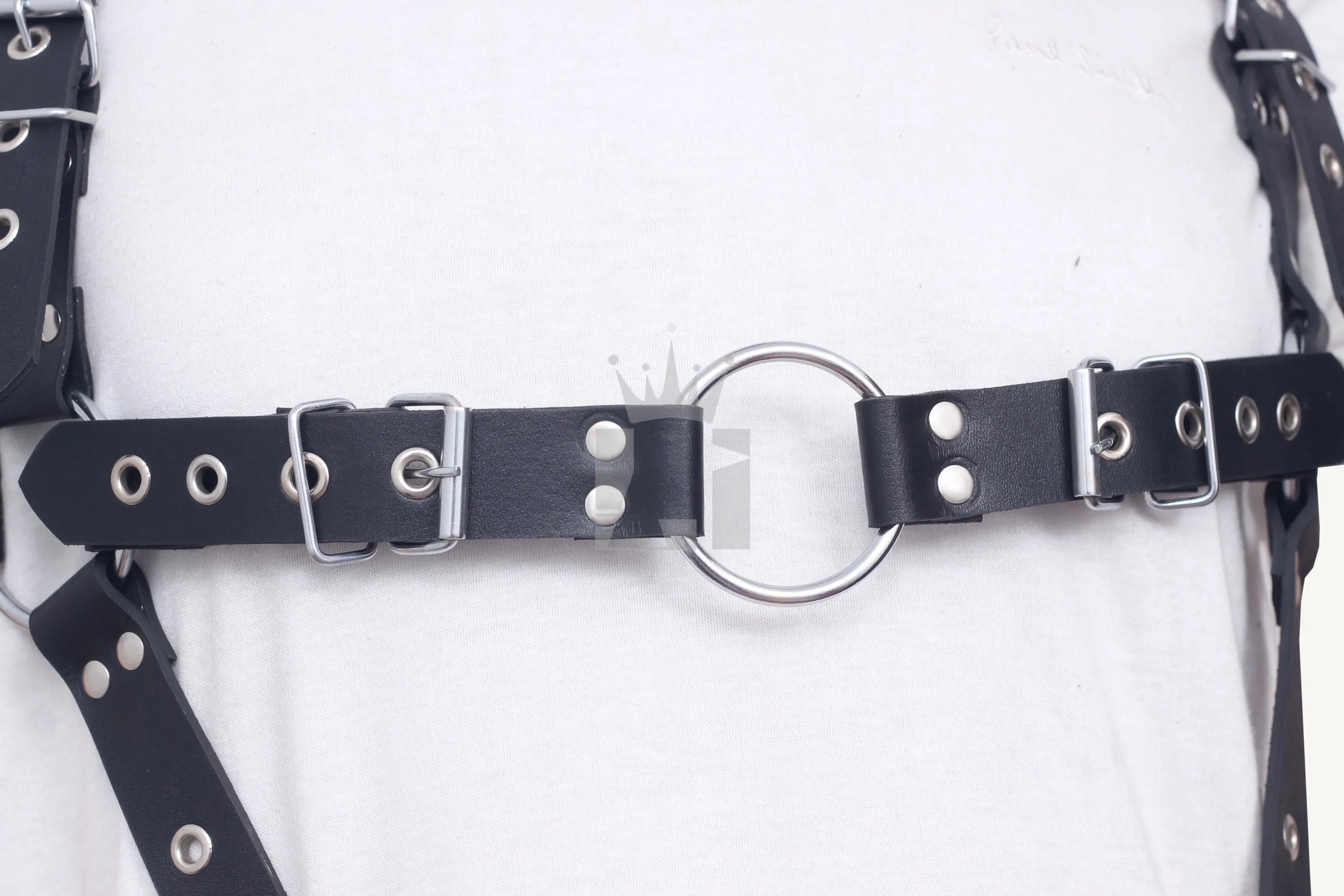 Close-up of silver buckle and O-ring detail on the chest strap of black leather harness.