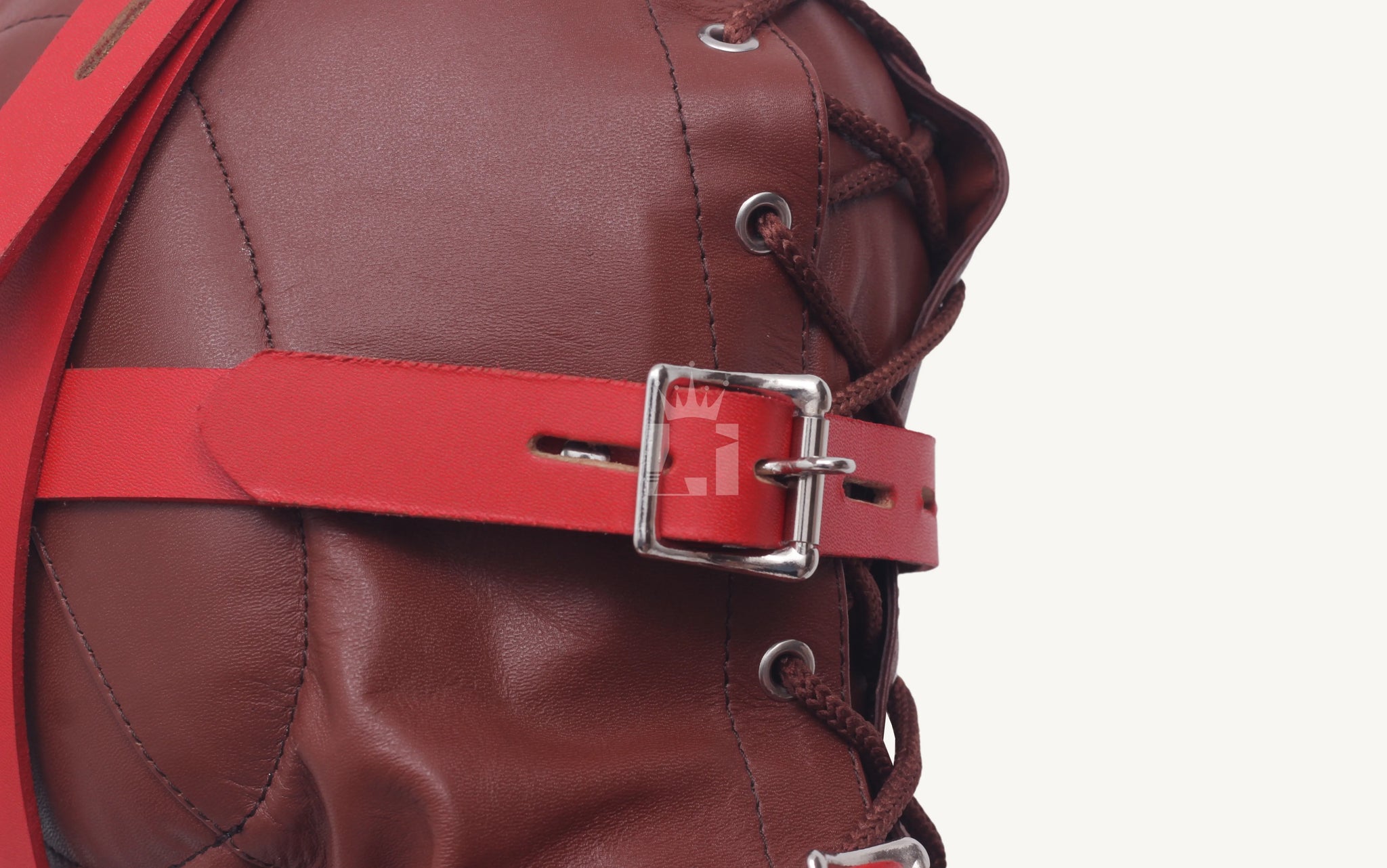 Detailed close-up of silver buckle fastening red leather strap on the bondage hood.