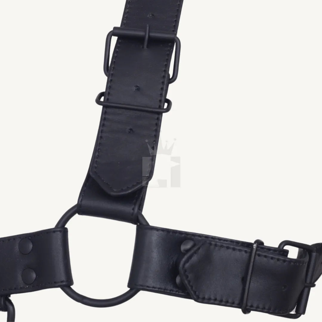 Detailed view of black leather chest harness showing adjustable strap and metal O-ring connection.