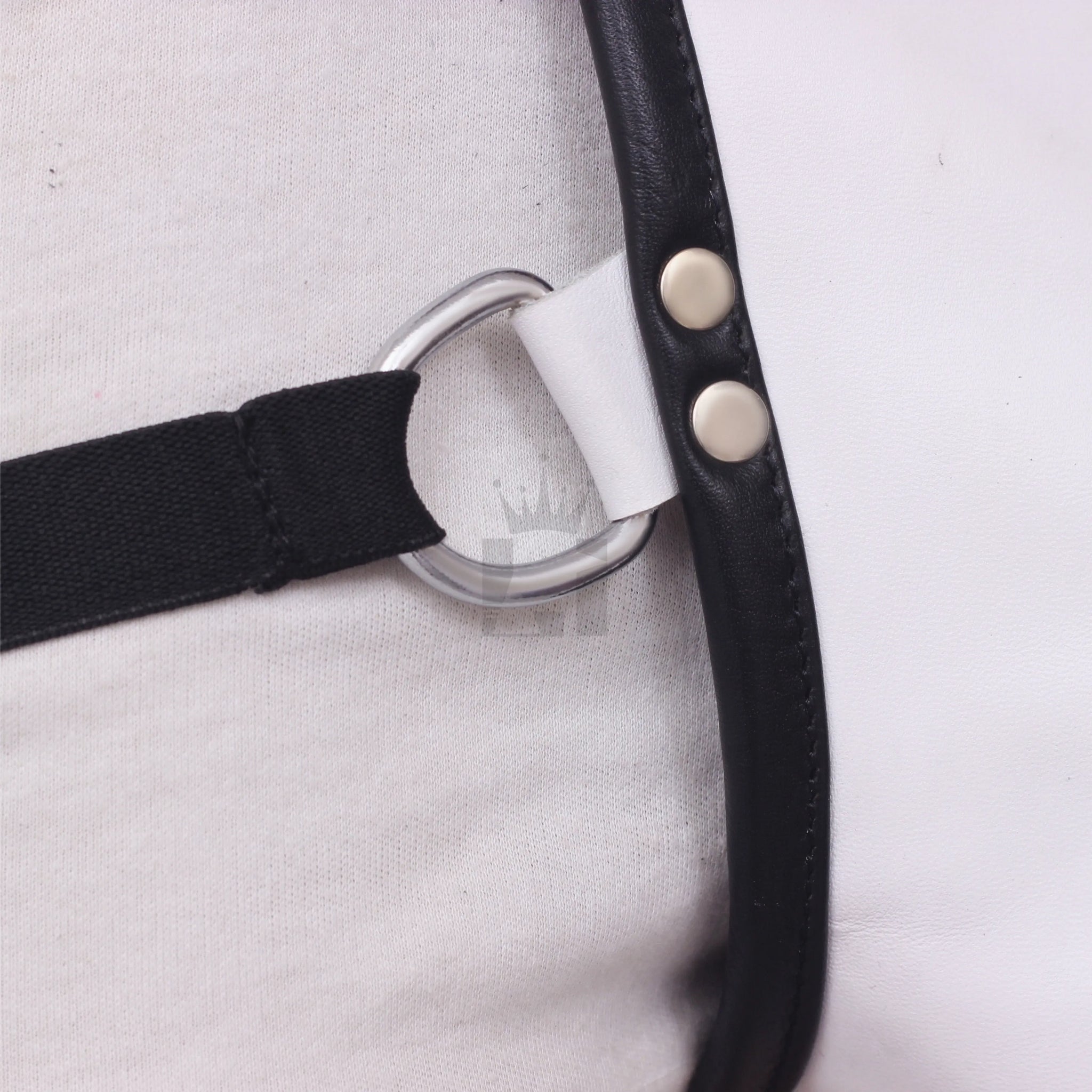 Detailed view of black elastic strap attached to silver D-ring with riveted white leather trim.