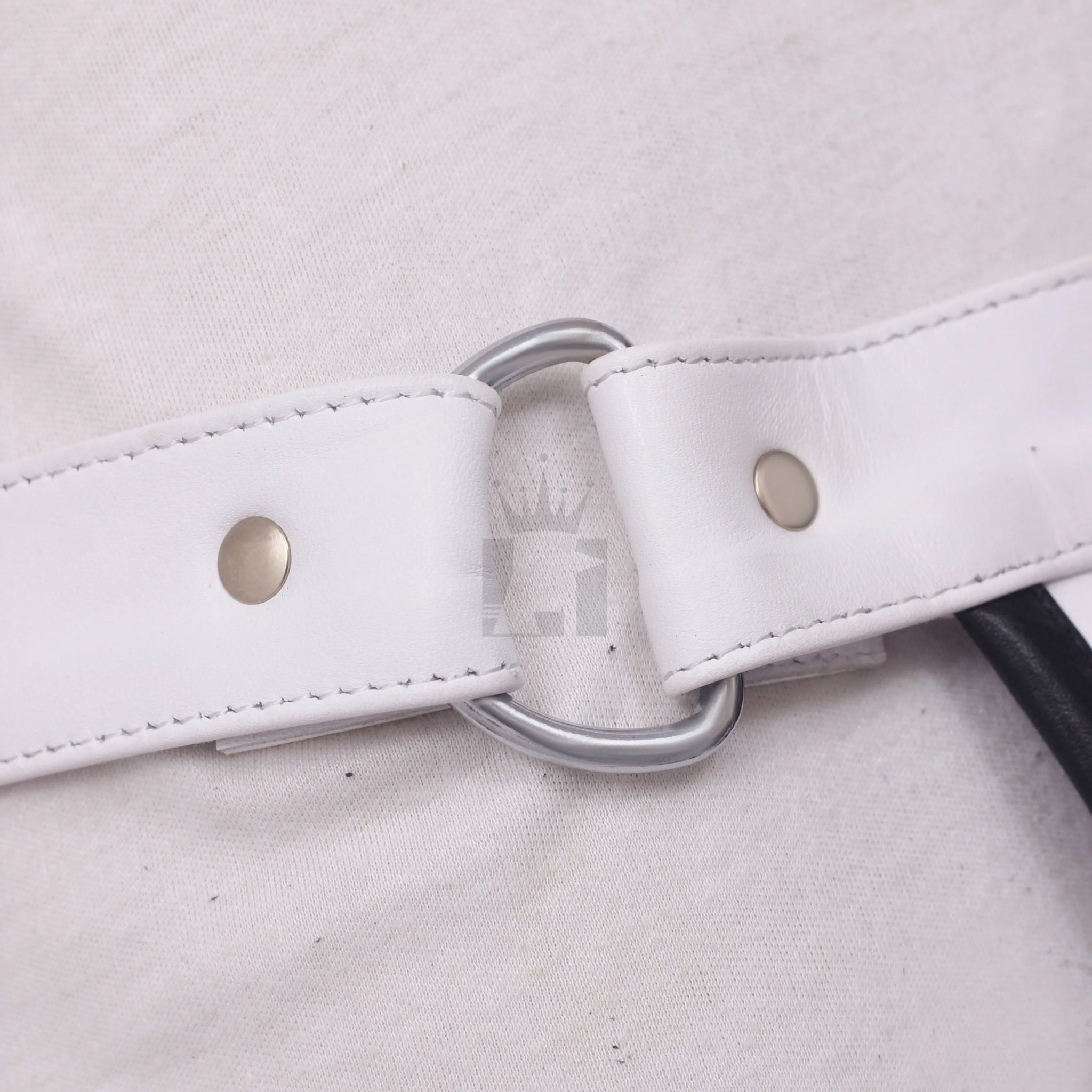 Detail shot of silver D-ring attached to white leather waistband with metal rivets.