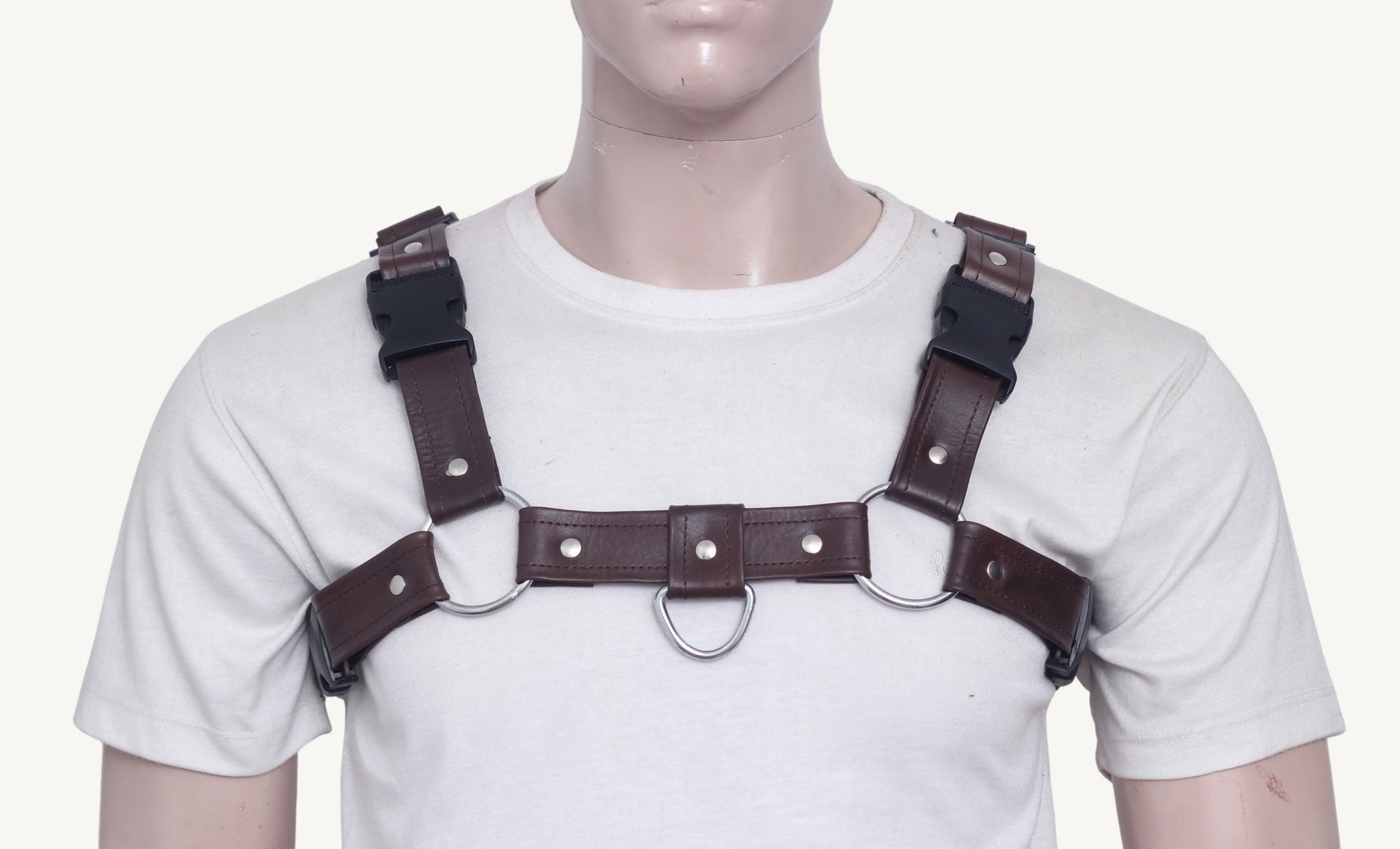 Front close-up of mannequin in brown leather chest harness with dual O-rings, center D-ring, and black buckle straps.