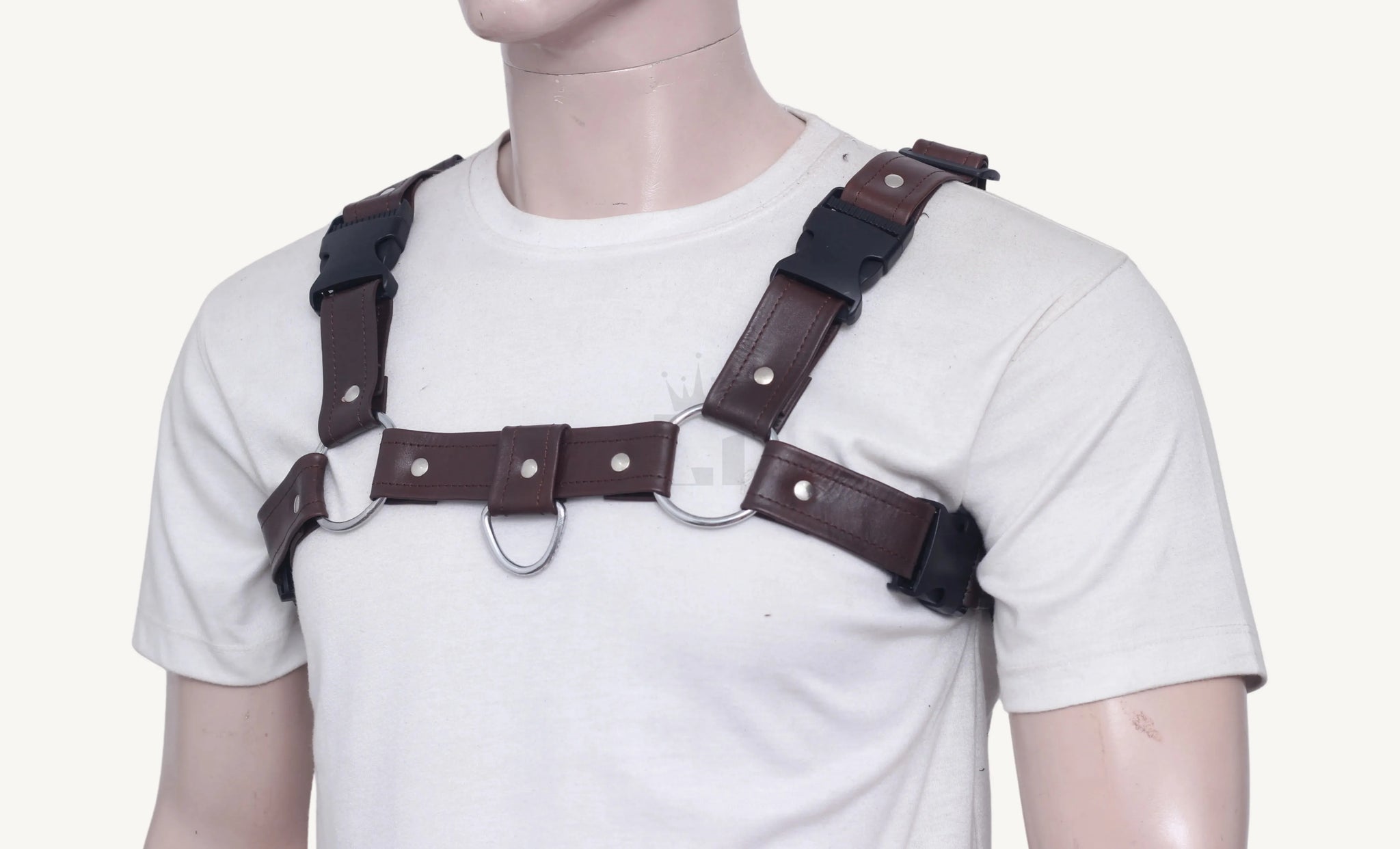 Mannequin wearing brown leather chest harness with silver O-rings and black buckle closures, front angle view.