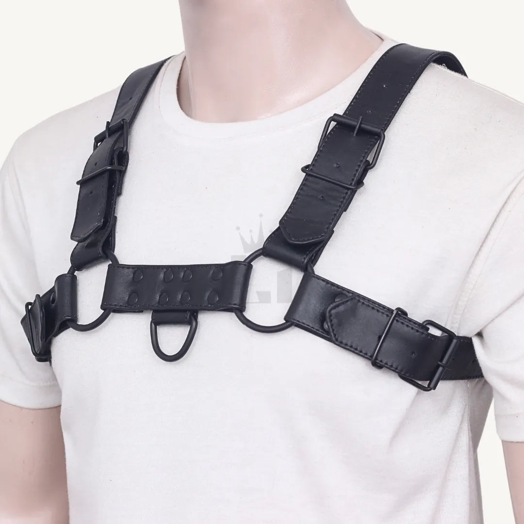 Front view of black leather chest harness with adjustable straps and O-rings worn over a white shirt.