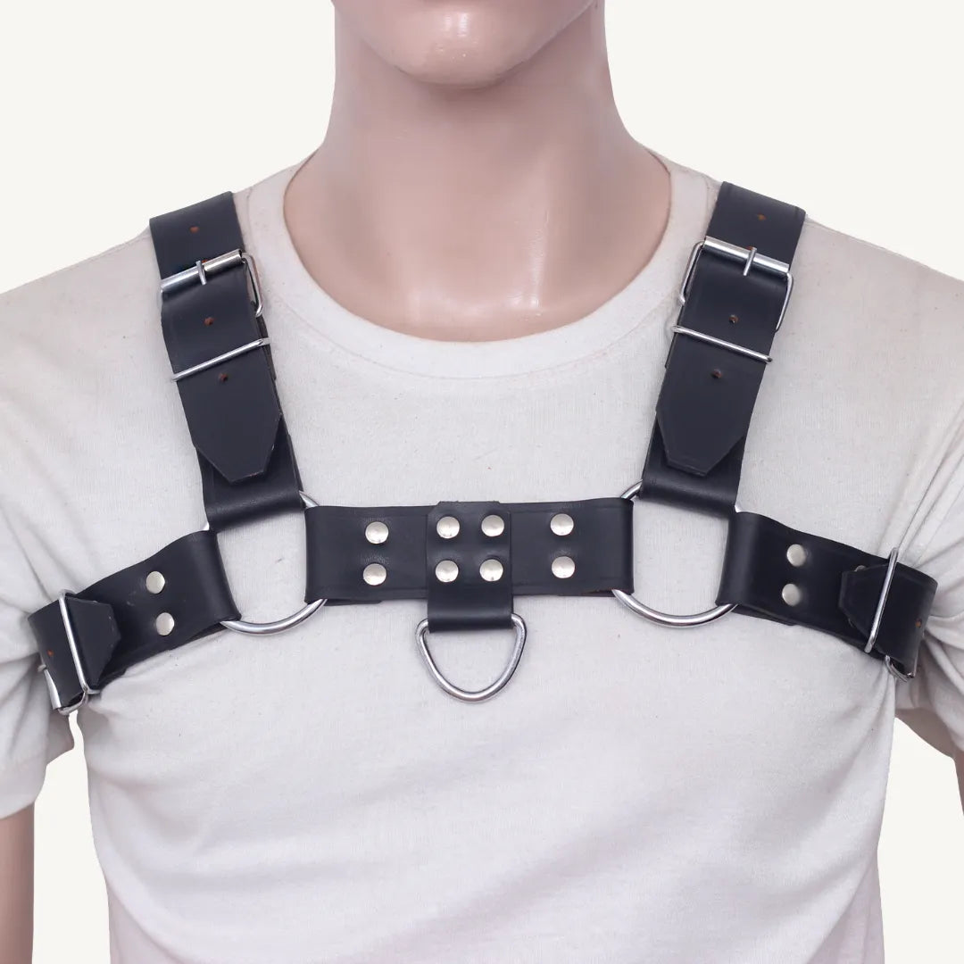 Straight front view of black leather chest harness with silver hardware, rivets, and center D-ring.