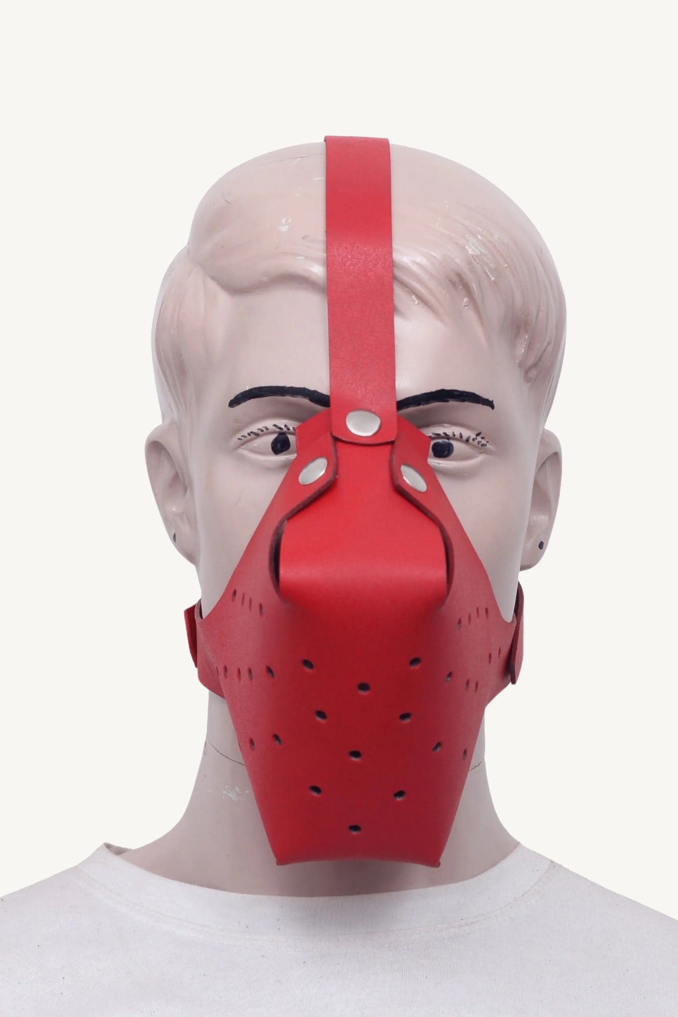 Front view of a mannequin wearing a red leather bondage muzzle with ventilation holes and forehead strap.