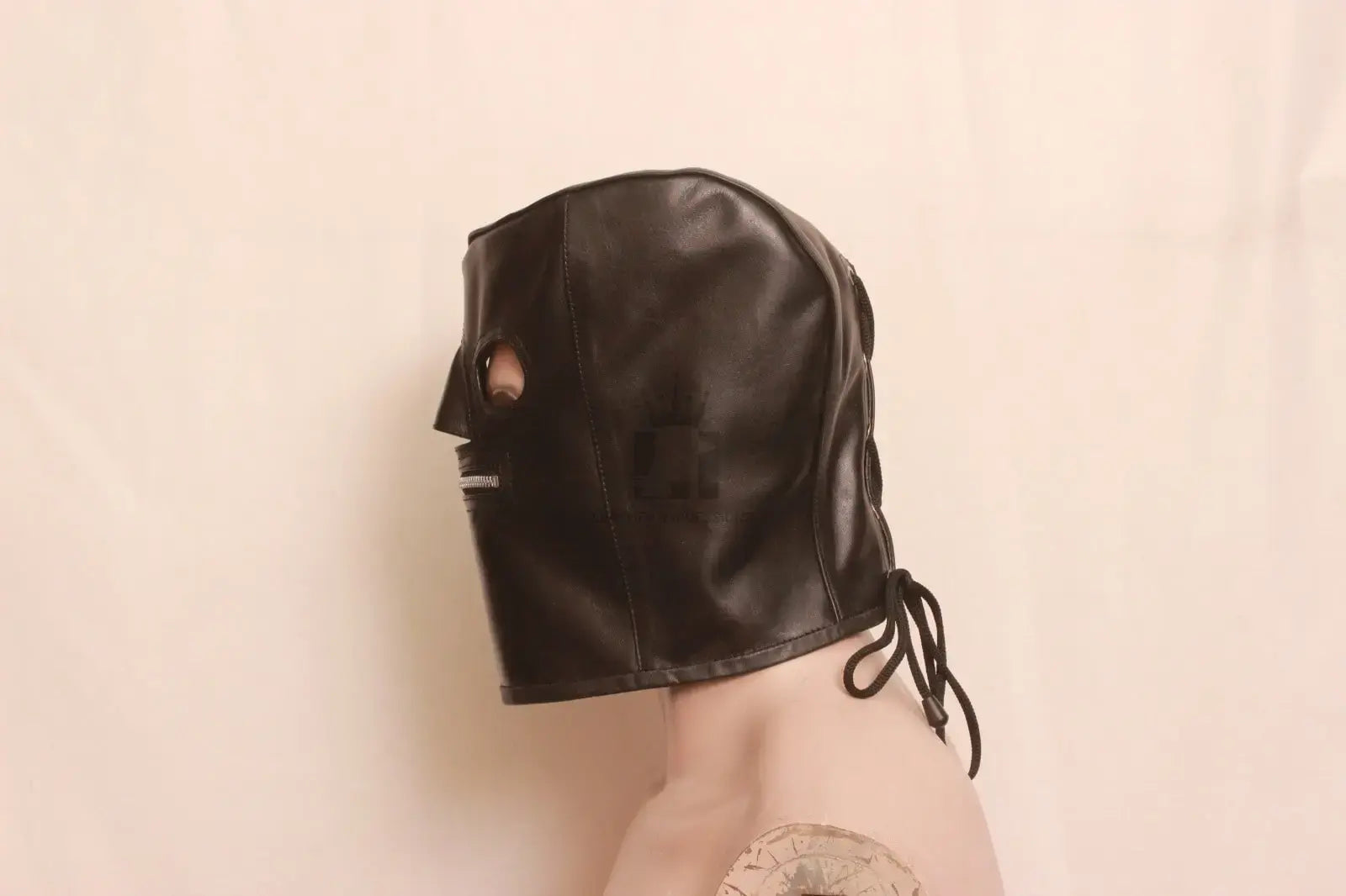 Left Side angle view of dummy wearing a black leather bondage hood with mouth zipper and laces on a white background.