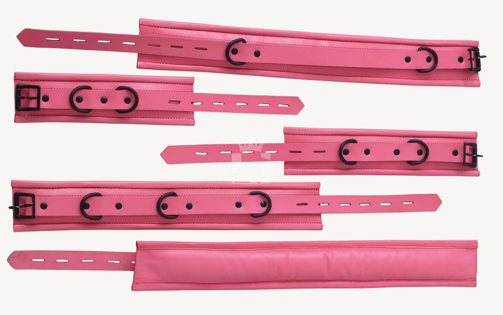 Top-down view of multiple pink leather BDSM cuffs with black buckles and D-rings, showcasing adjustable holes and padded interiors for secure and comfortable BDSM restraint.