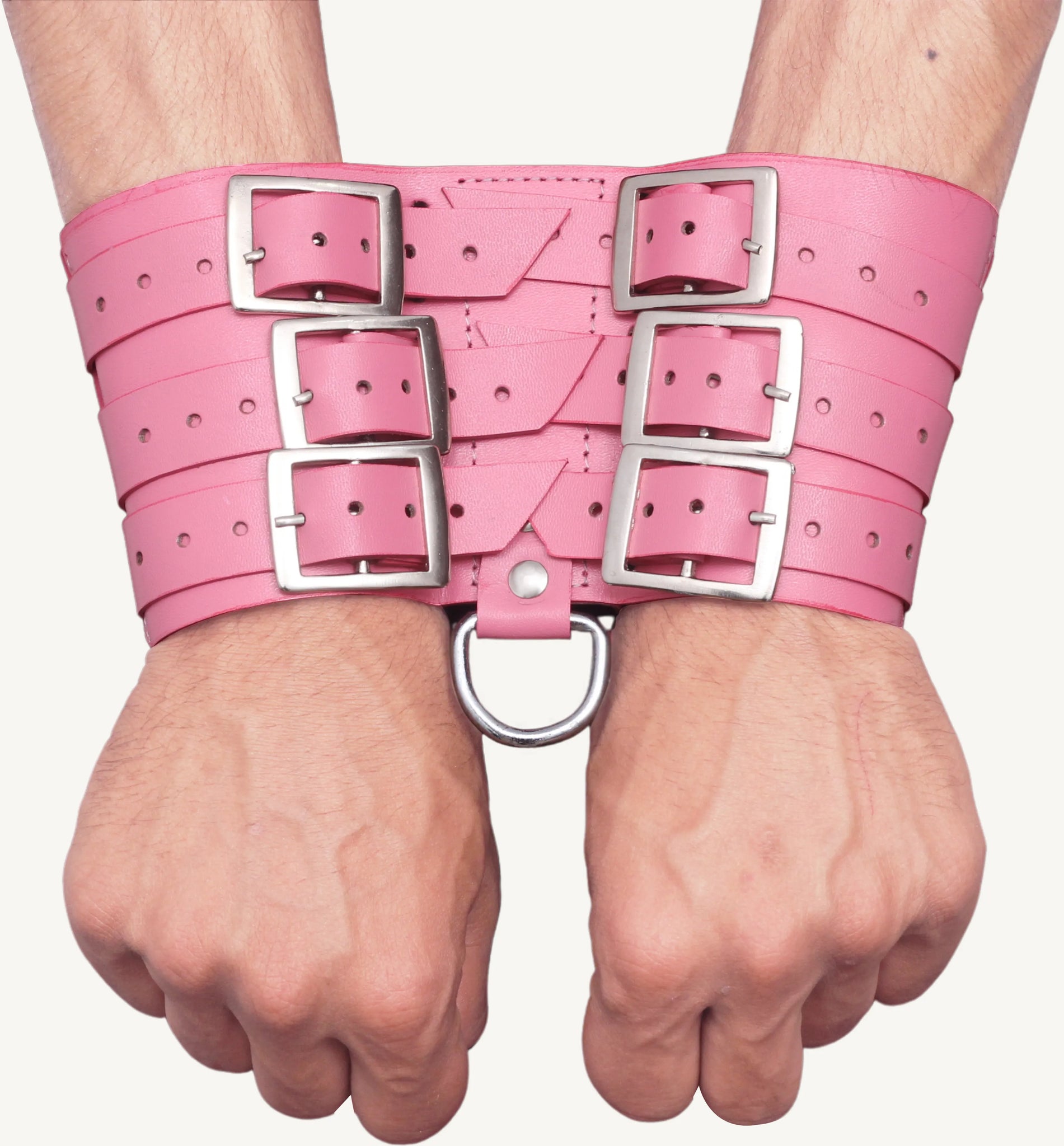 Close-up of pink leather handcuffs strapped on wrists, featuring six metal buckles and a sturdy D-ring.