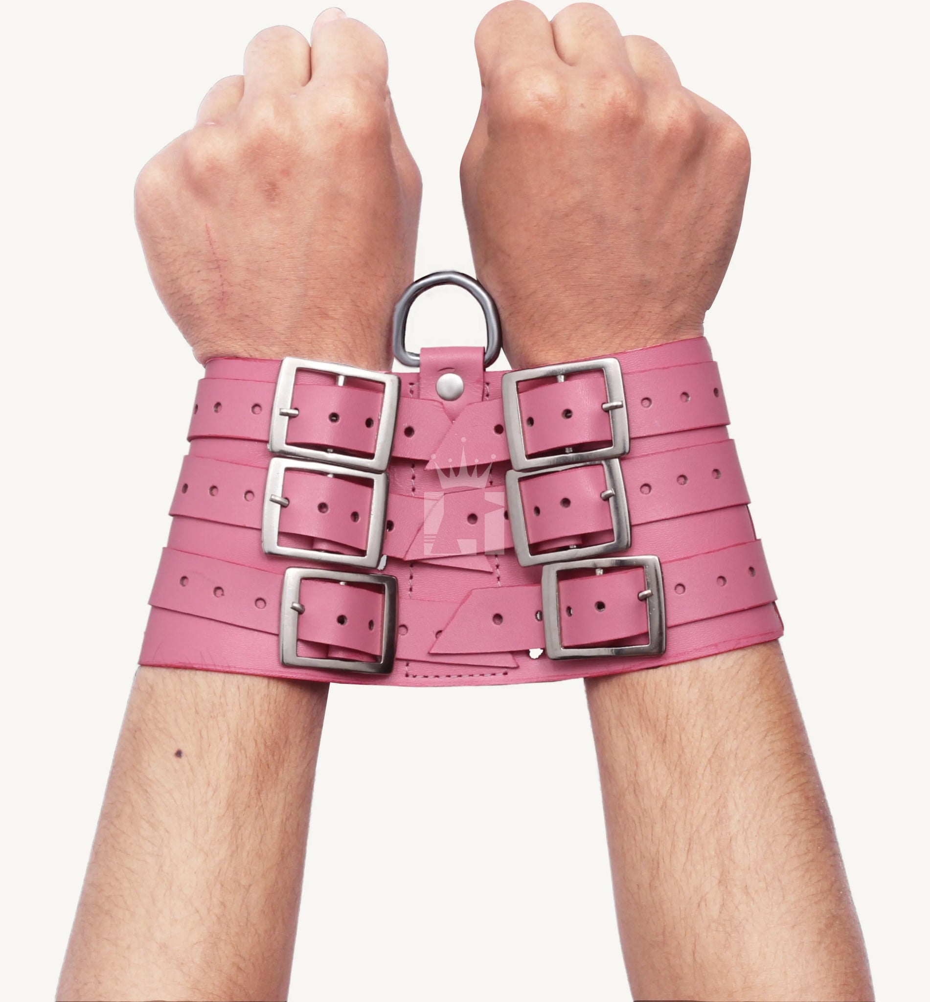 Pair of hands wearing pink leather wrist cuffs secured with multiple buckles and a steel D-ring for bondage play.