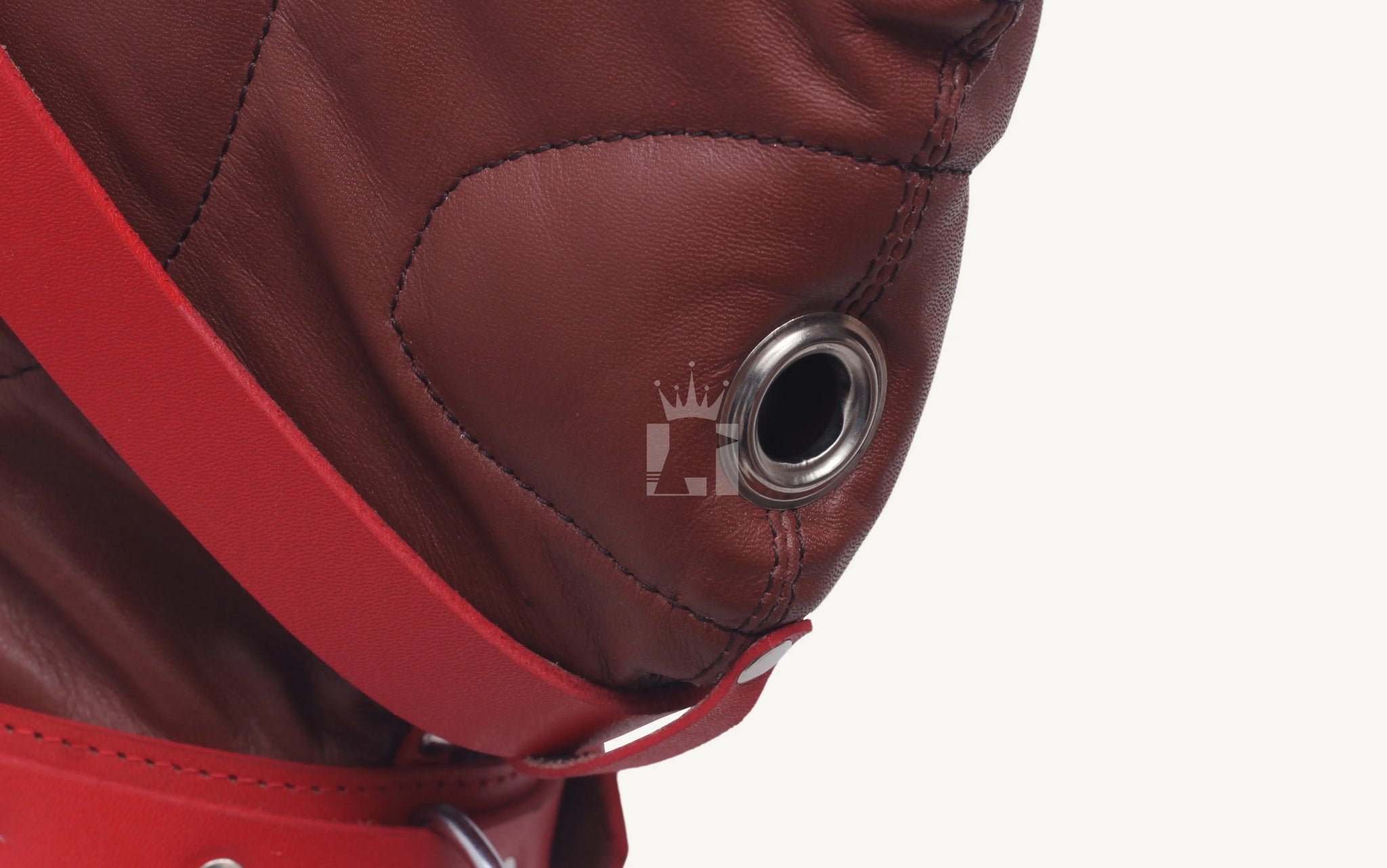 Close-up of metal breathing hole on brown leather Bondage hood with red strap detail.