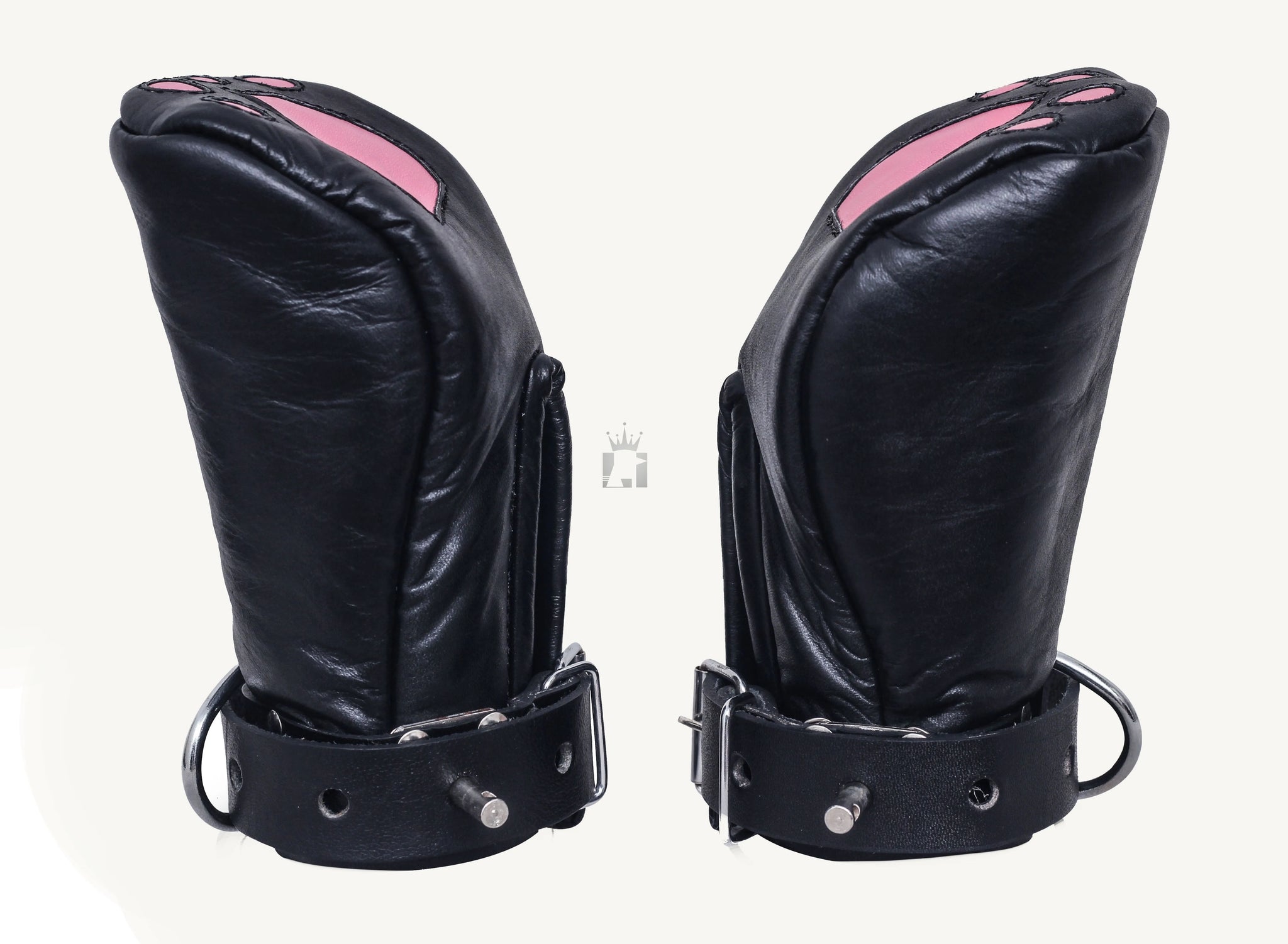 Front view of a handmade black leather bondage mittens on side angles designed to resemble cat paws, featuring pink paw pad designs on the top side. The mittens have a rounded, padded shape with buckled leather straps at the wrists, suggesting a secure fit.