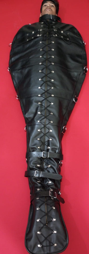 font angle view of a horizontal boy laying on a red surface wearing a handmade leather bondage sleepsack with straps