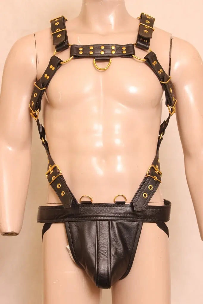 front angle view of a dummy wearing black leather chest harness with jockstrap and golden nickels on it in off white background