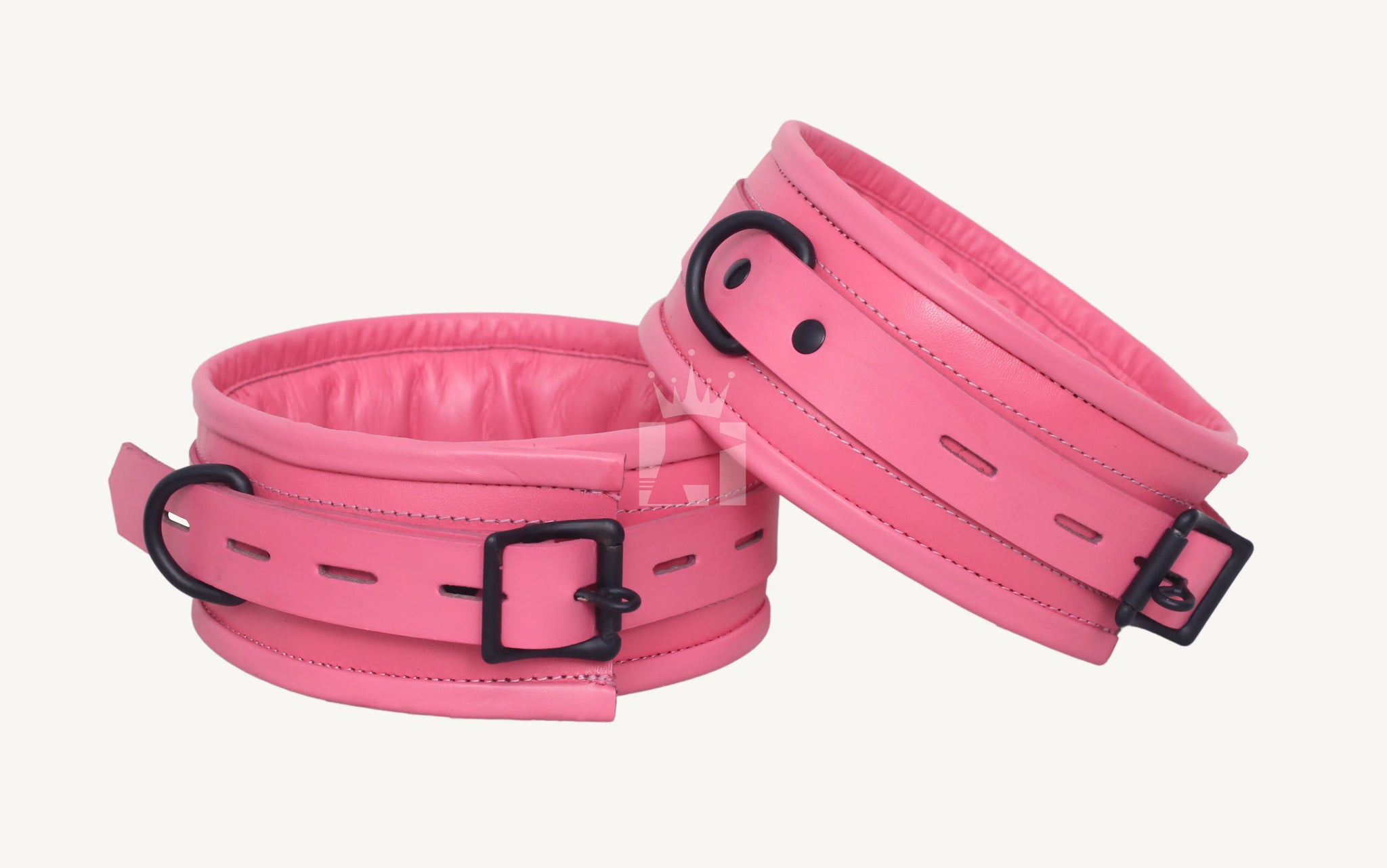 Close-up angled view of pink bondage cuffs featuring padded interiors, black metal buckles, and D-rings, designed for comfortable restraint in BDSM play.