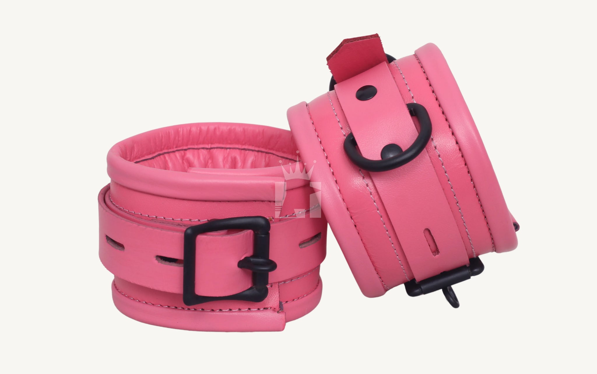 Close-up angled view of pink leather handcuffs featuring padded interiors, black metal buckles, and D-rings, designed for comfortable wrist restraint in BDSM play.