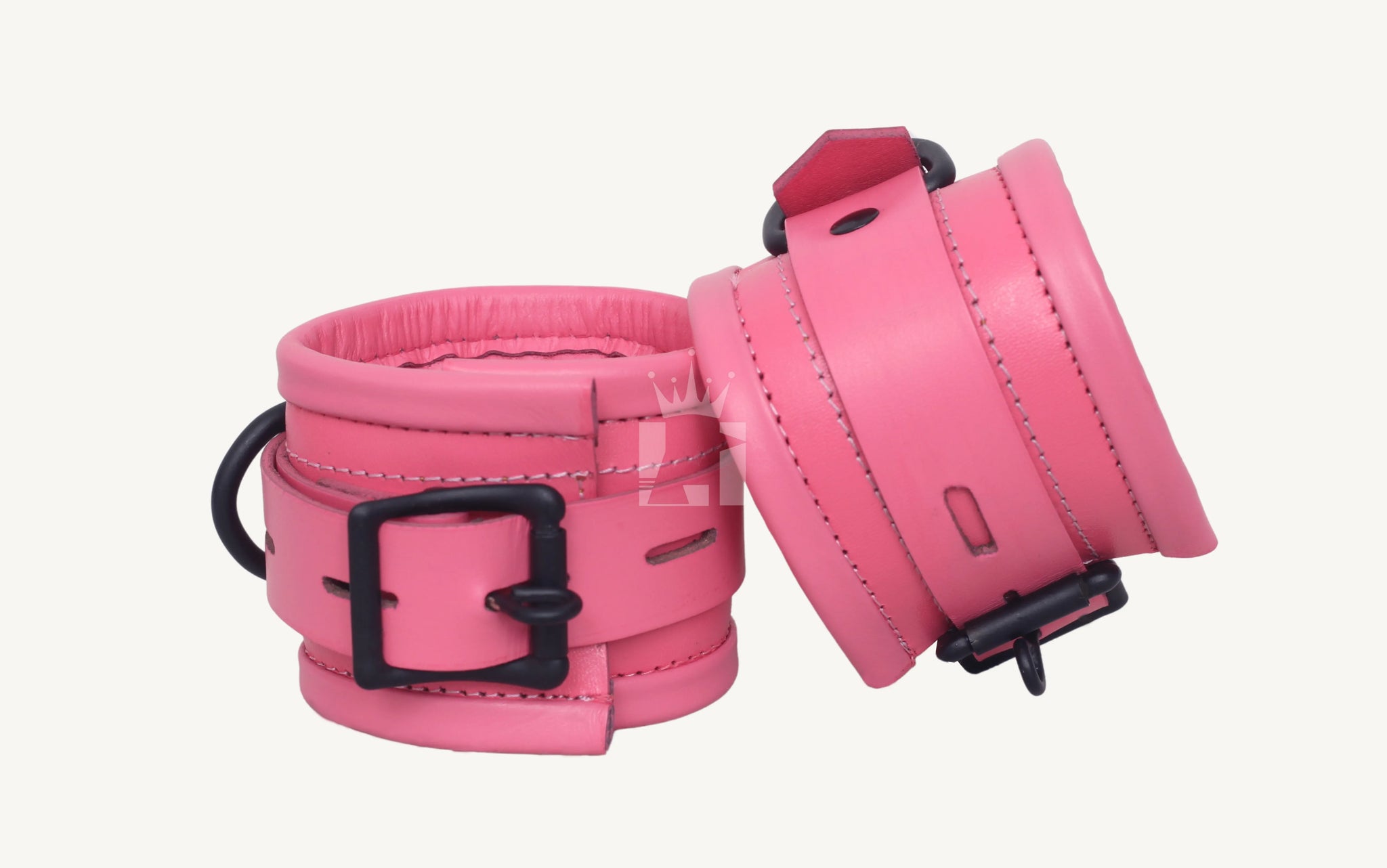 Close-up angled view of pink leather bondage handcuffs featuring padded interiors, black metal buckles, and D-rings, designed for comfortable wrist restraint in BDSM play.