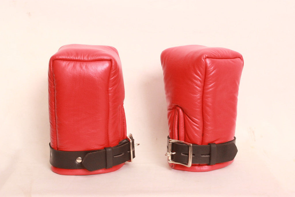 A pair of red padded leather bondage mittens with black leather straps on a plain white background.
